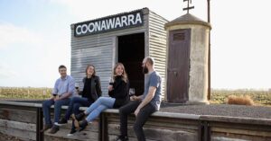 four people sit on a railway at the Coonawarra siding drinking red wine and laughing