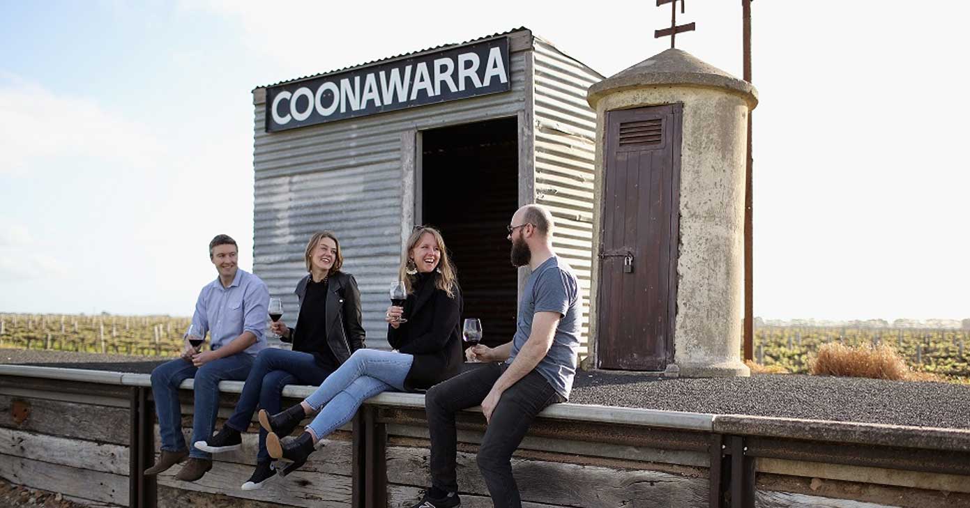four people sit on a railway at the Coonawarra siding drinking red wine and laughing