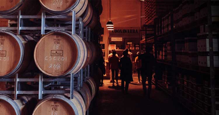 people walk down dimly lit winery museum area