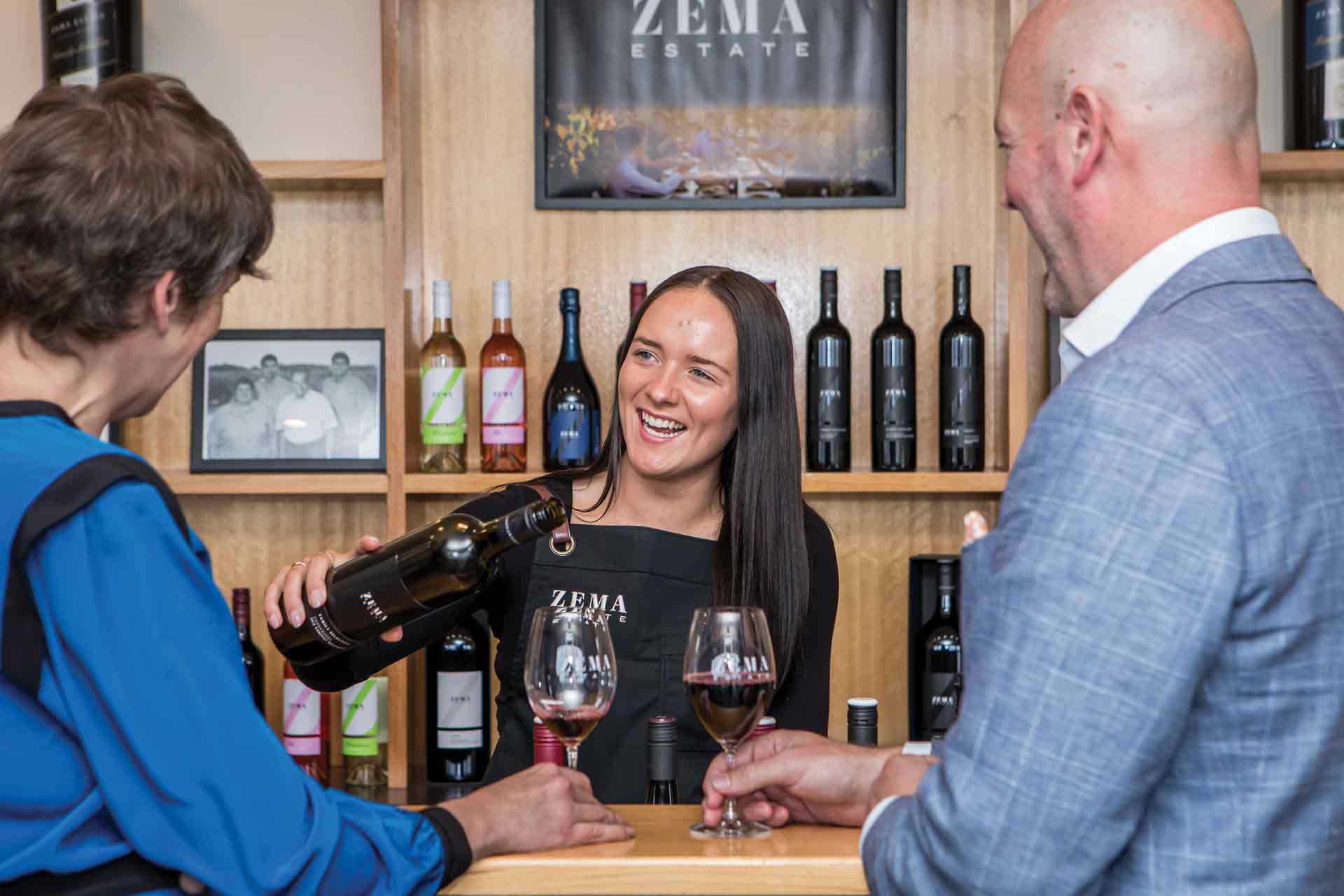 lady smiling and serving wines to two people in cellar door